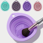 Purple silicone brush cleaning dish with a brush inside, surrounded by smaller silicone dishes in different colors on a light gray background.
