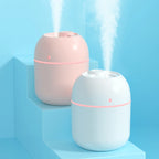 Two humidifiers, one pink and one white, emitting mist on a light blue background.