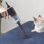 Person using a handheld vacuum cleaner on a blue surface with a cat observing.